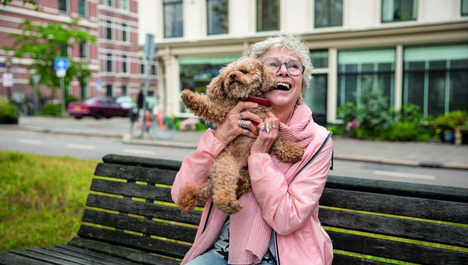 Dam som lyfter upp hunden på parkbänken