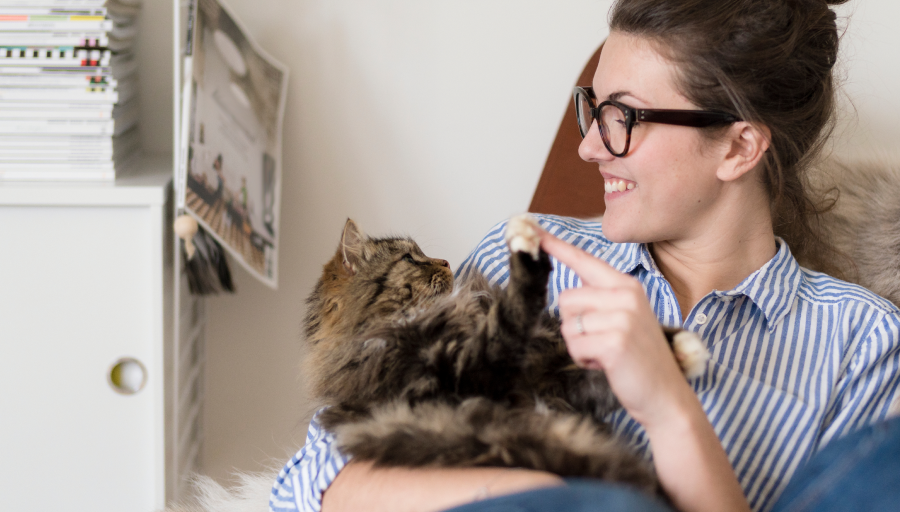 En kvinna sitter med sin katt i knät och tar på kattens tass med sitt finger.